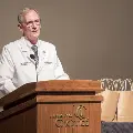Man in white coat speaking at podium